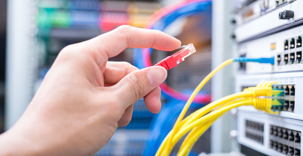 Les mains d'un technicien testent un câble Ethernet sur une prise murale, arrière-plan de bureau flouté